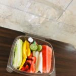 A fresh fruit salad in a to-go container, featuring a colorful mix of fruits such as strawberries, blueberries, and pineapple
