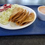 Tacos filled with radishes, cabbage, and sauce, served on a blue tray, offering a colorful and appetizing Mexican dish